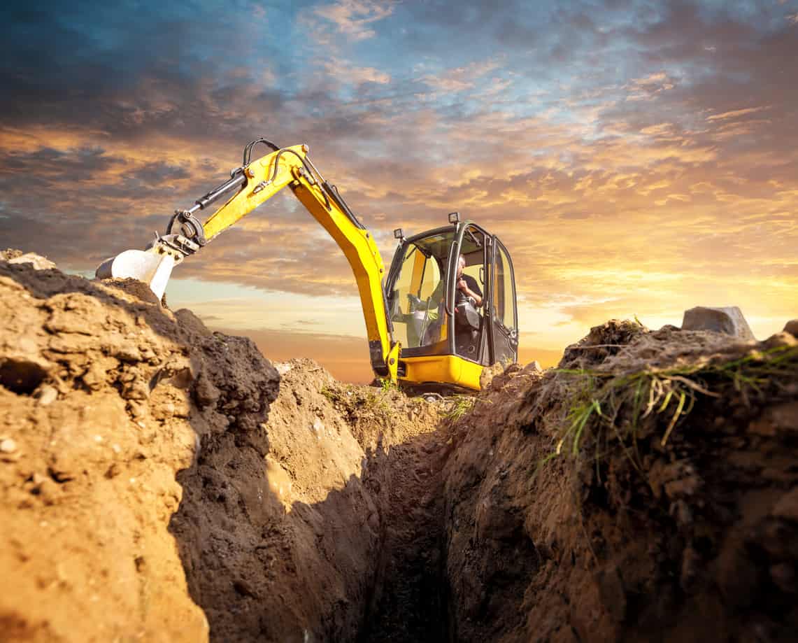 Mini excavator digs down in the background of the sunset